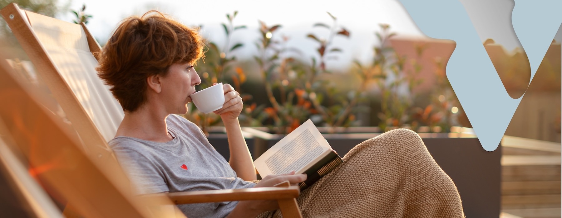a woman lounging outside reading a book and drinking coffee